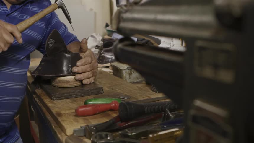 A man is using a tool to repair a shoe on a bench