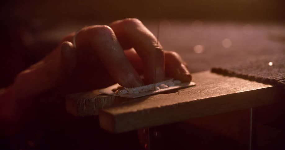 Person holds small item while sawing on it in workshop