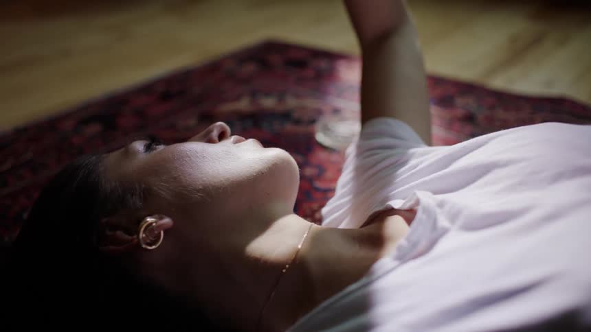 A woman lays on the floor playing with the sunlight, blocking it out of her eyes with her hand.