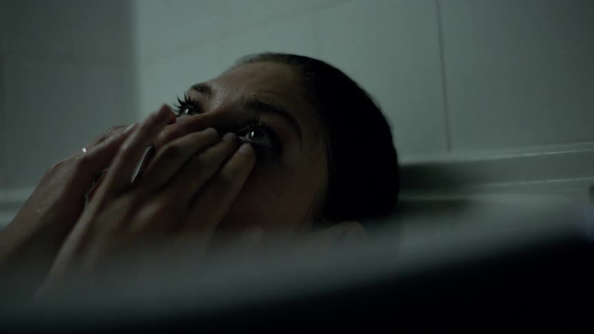 A woman lying in a bathtub wipes her eyes as she cries