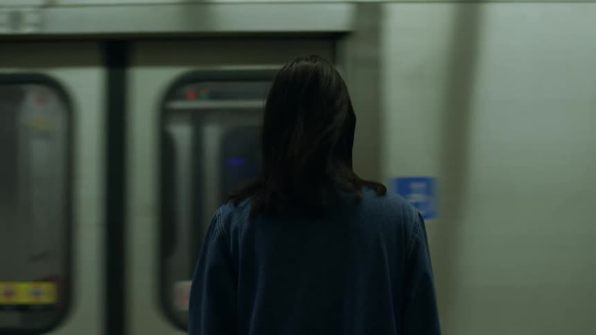 A subway train stops in front of a woman in the station