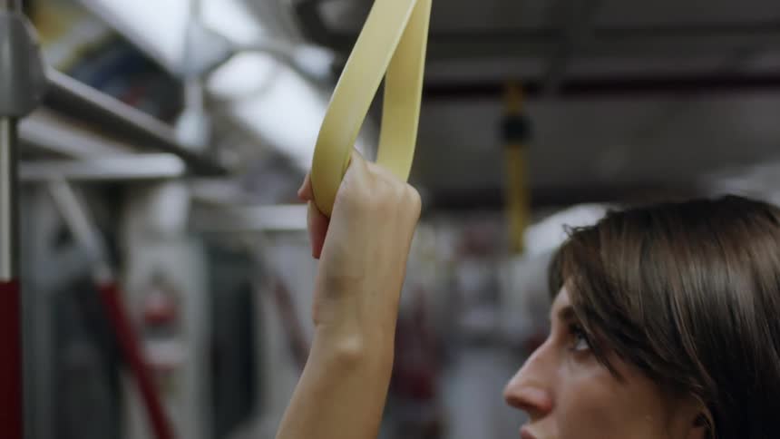 A woman stands holding the strap on a subway train