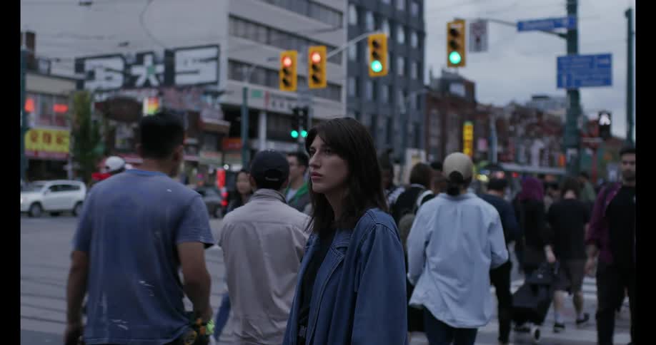 A woman stands in a busy crosswalk at a city intersection as pedestrians walk around her