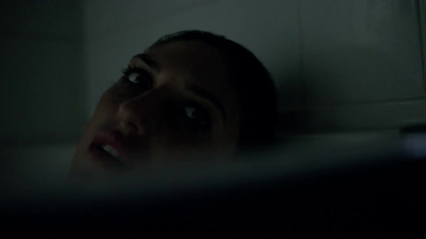 A woman in a bathroom laying in the bathtub with the light swinging