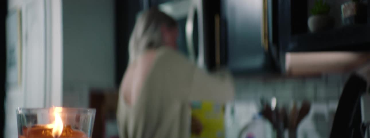 A woman bakes in a kitchen with a candle burning on the counter