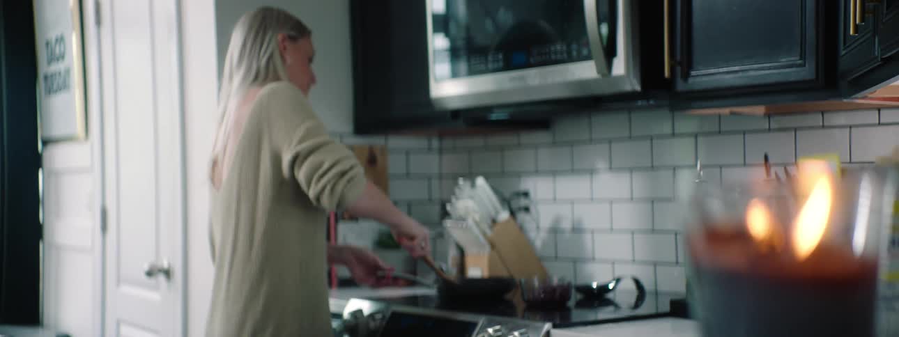 Blonde woman with a white sweater cooks on the stovetop in the kitchen