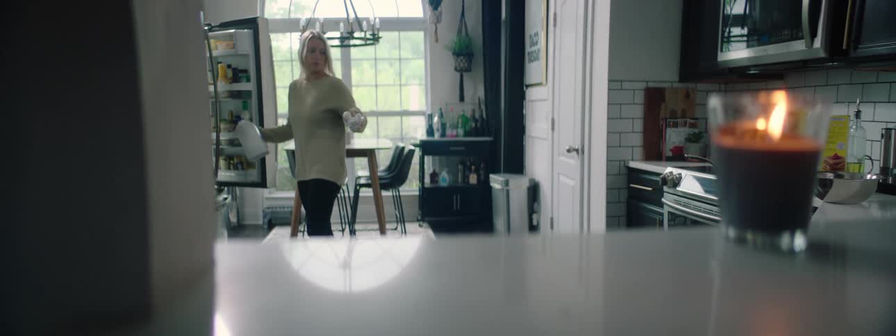 A woman in the kitchen opening a fridge and taking eggs and milk