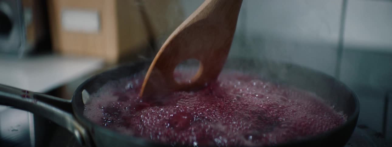 A pan boiling cranberry while being mixed with a wooden spoon