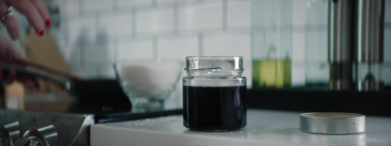 A woman using a wooden spoon to scoop syrup from a pan into a jar