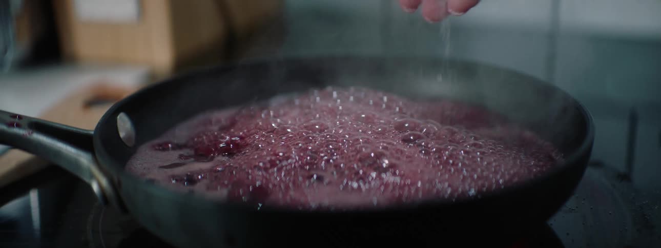 A purple liquid boils in a skillet as a person sprinkles salt over it