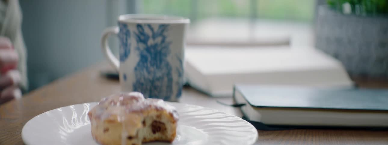 A woman puts a scone with a bite out of it on a plate before picking up her coffee mug