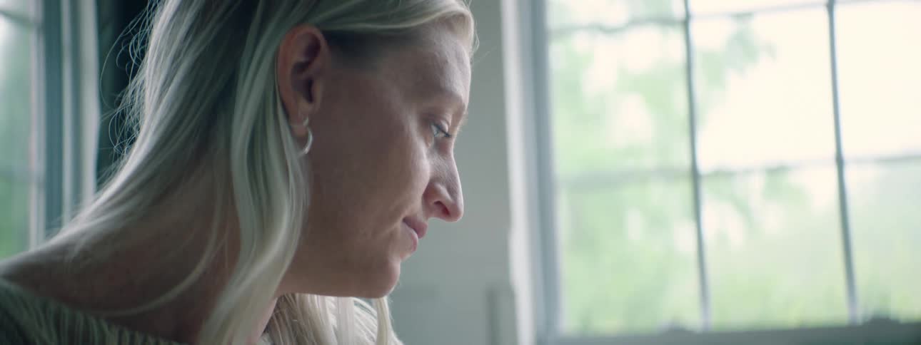 A white woman in front of a window turns her head and smiles