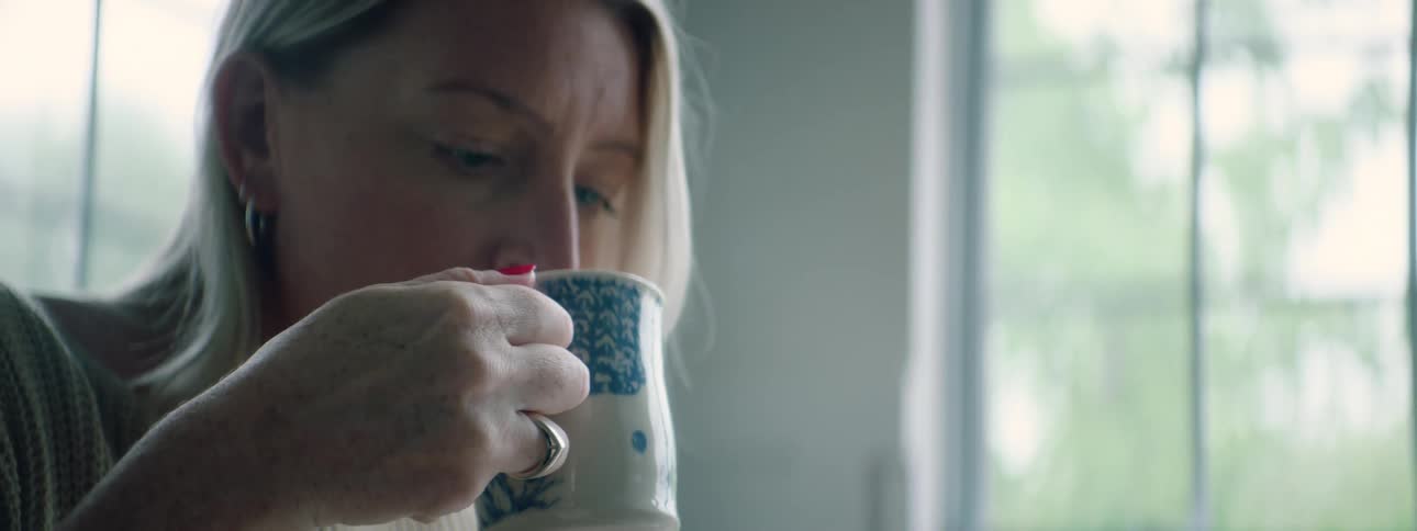 A woman sits at home and reads and drinks a coffee