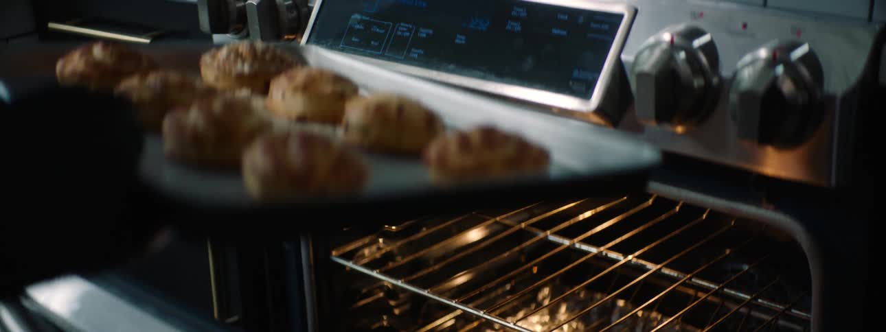 A person in a kitchen with gloves taking pastries out of a oven