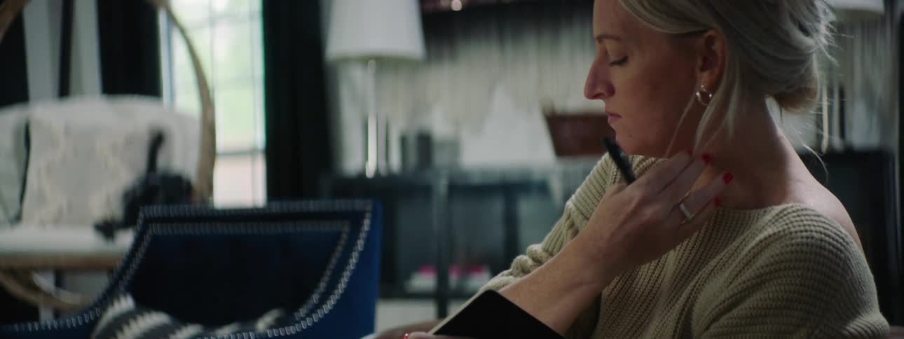 A woman sitting on a sofa pets a dog before beginning to write in a notebook