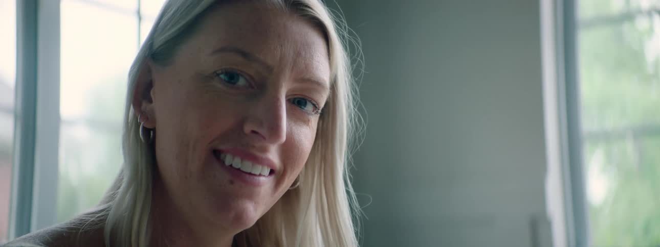 A woman in a room staring and smiling with windows in the background