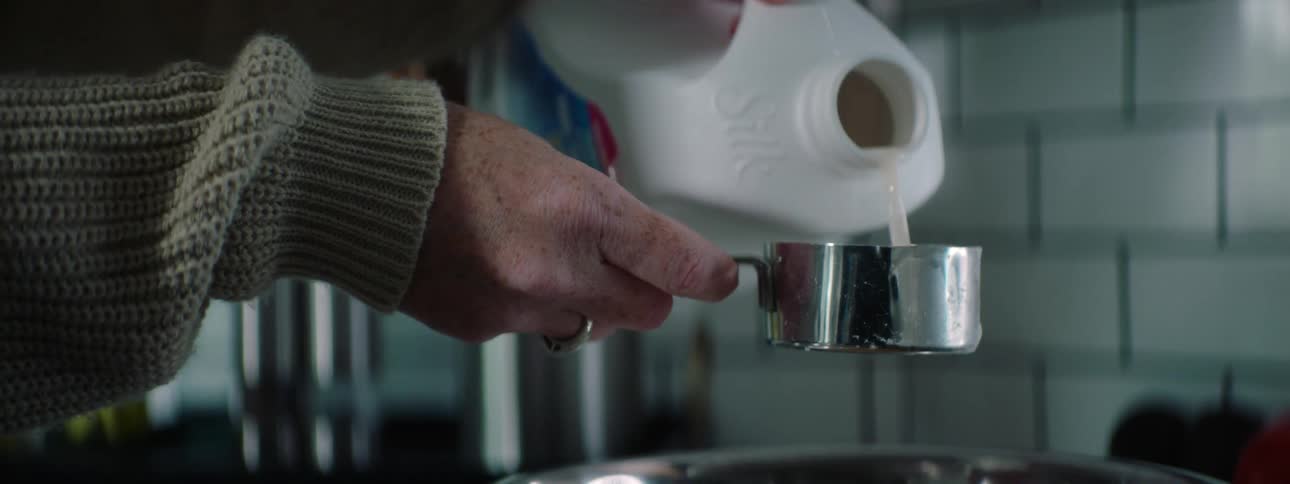 A woman carefully pours milk into a metal measuring cup then pours it into a mixing bowl