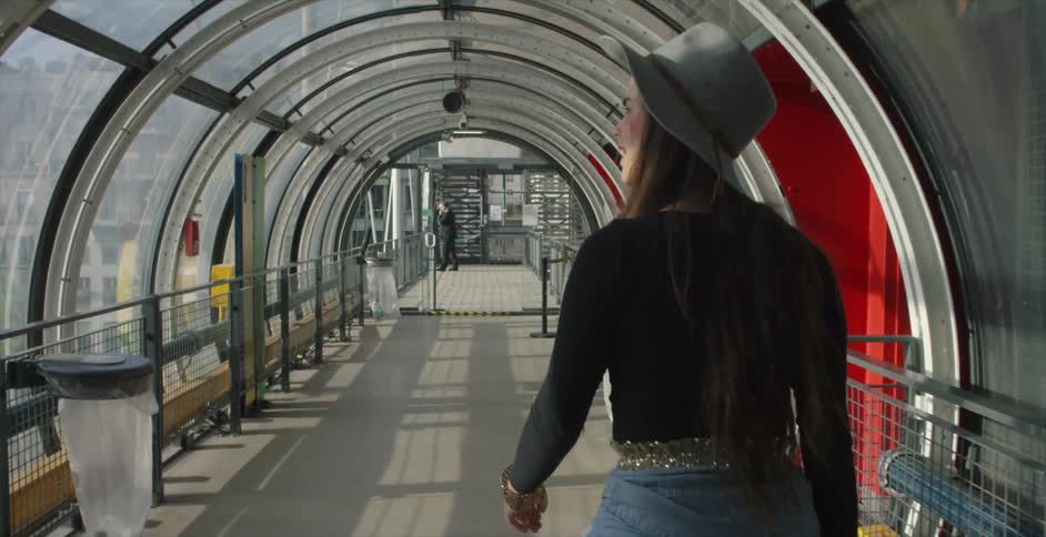A woman is walking down a hall looking out the windows as she goes