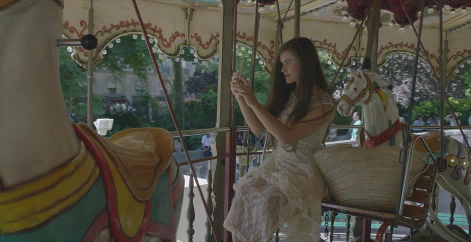 A woman sits on a carousel alone on a clear day