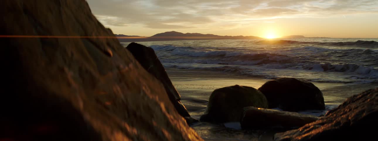 The sun peaks from below the horizon to shine on the tide as it washes onto a rocky beach