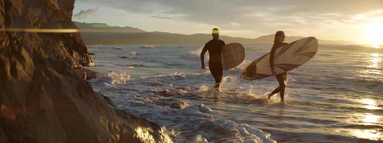 A man and woman run along the shore carrying surf boards