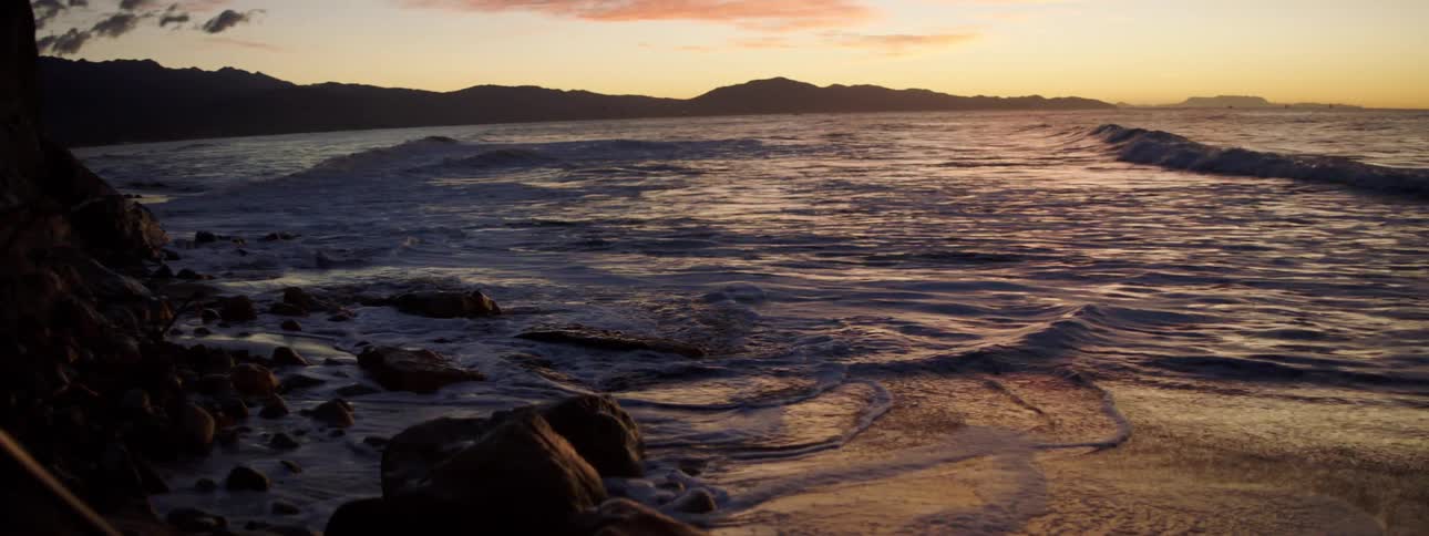 Ocean waves crash against a shore at sunset