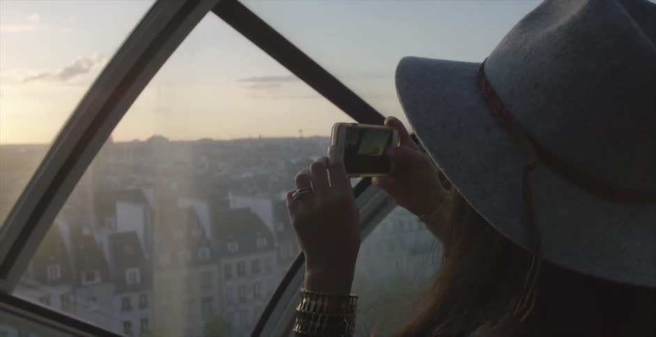 A woman takes a picture or video with her smart phone from a window