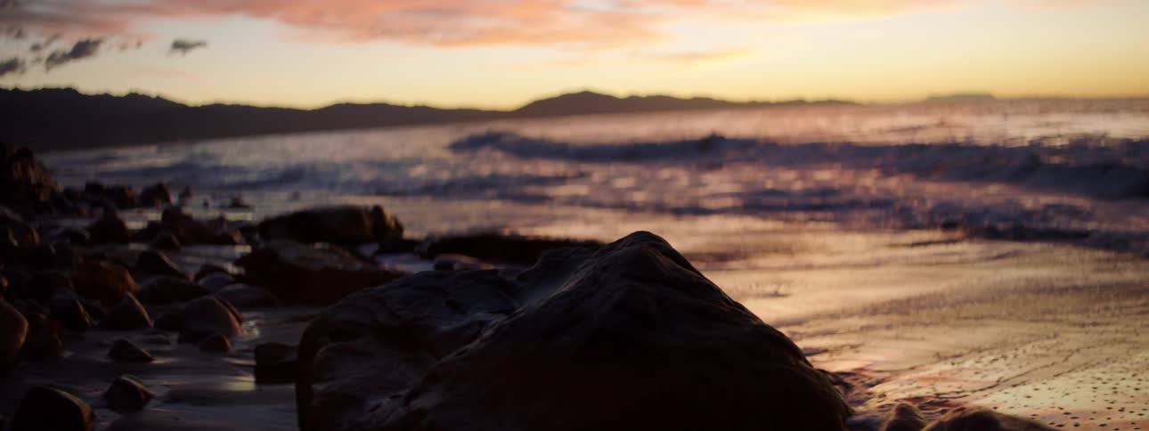 A beach with sand and rocks with the sky and clouds in the background