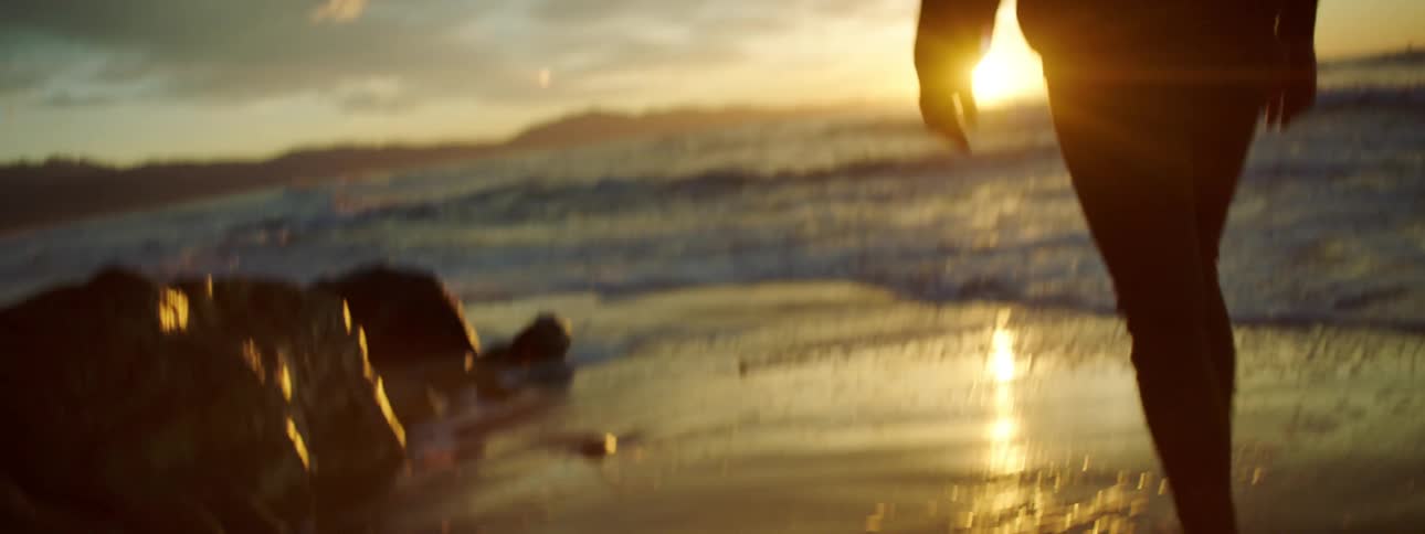 Man walks barefoot on the beach at sunset next to the sea