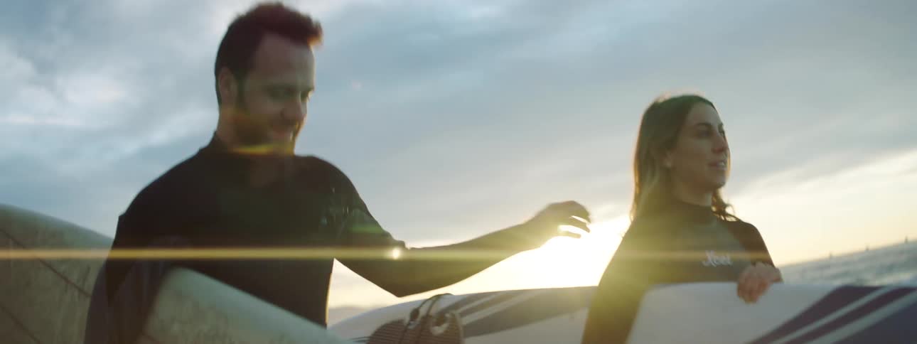 A man and woman walk near the ocean with surfboards