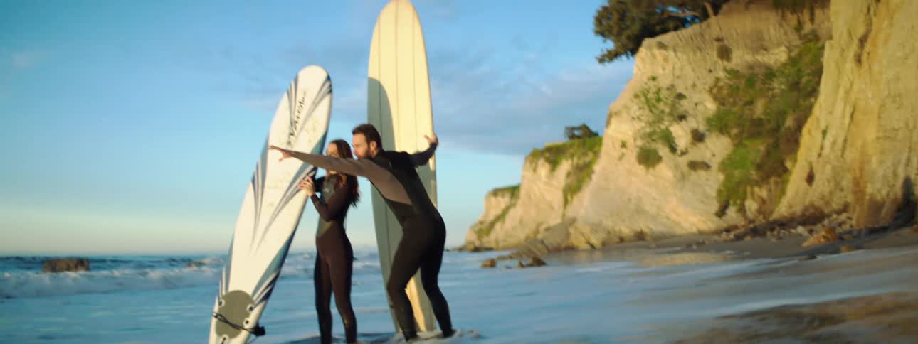 Man and woman with surfboards stand at the edge of the ocean