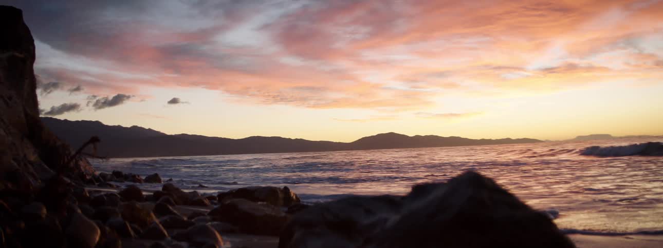 Strong waves crash into a beach embankment at sunset