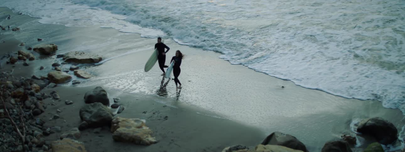 Two people run from the water with surfboards