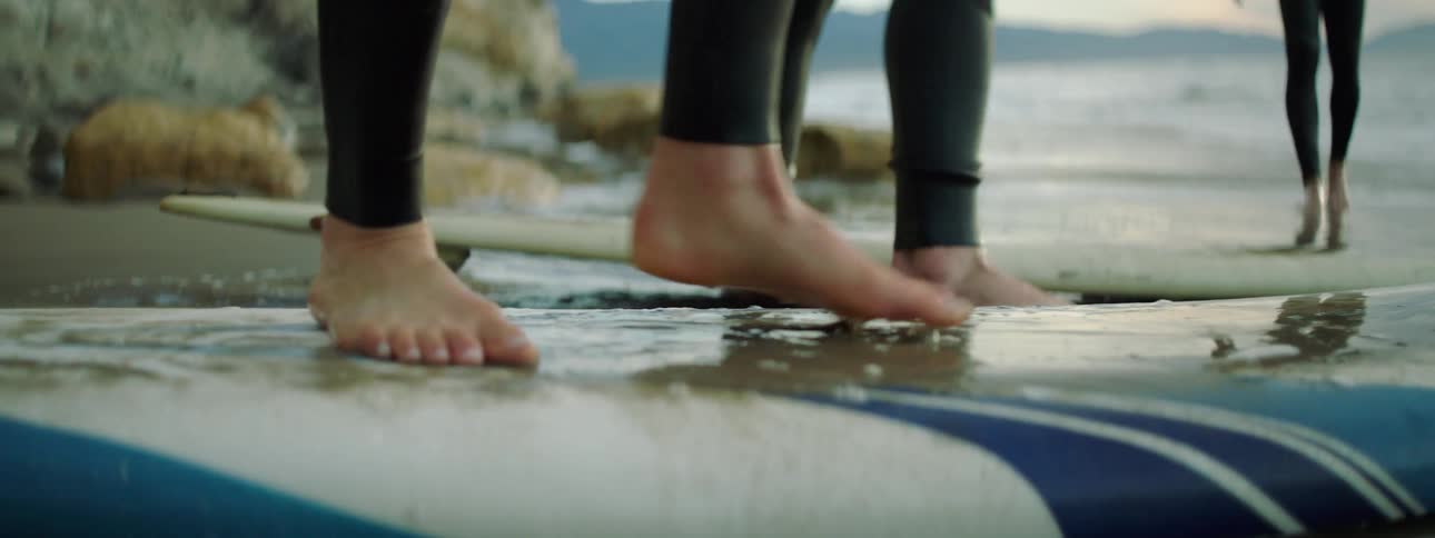 People standing on surfboards lying on the sand of a beach next to the water