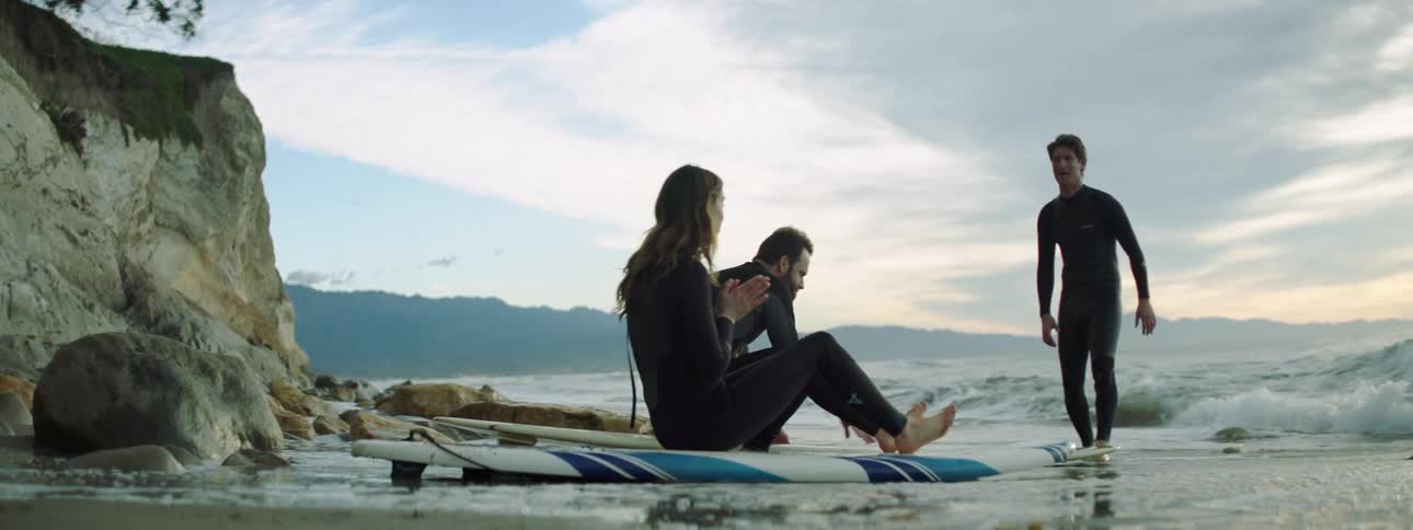 A couple on the shore with surfboards listen to an instructor