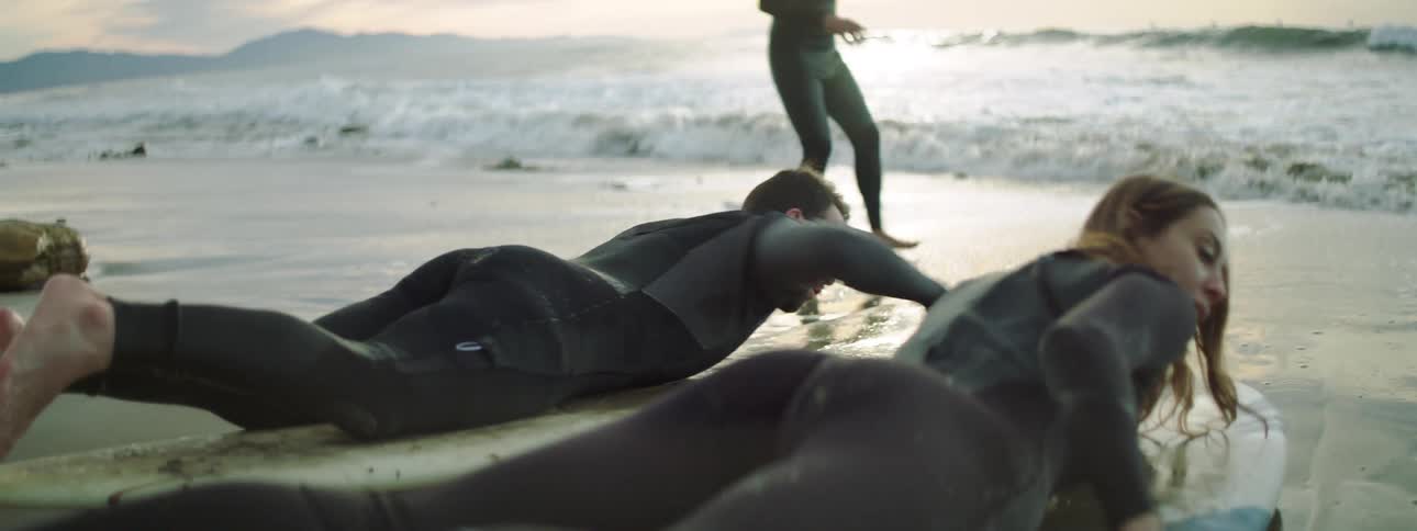 Couple paddling on a surfboard on the sand near shoreline at the beach
