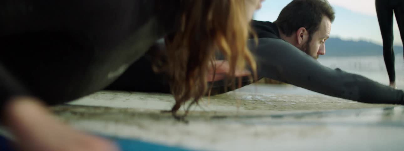 A female and male surfer practice surfing while on the beach as an instructor watches over them