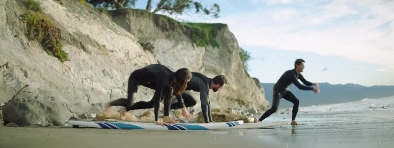 A man instructs two people on surf boards on the shore