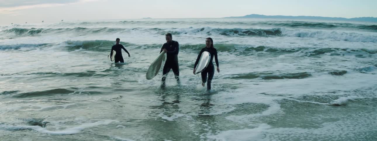 Three surfers carry their surfboards out of the water