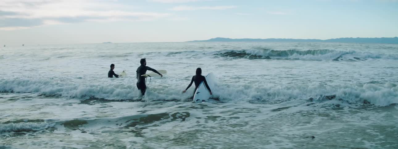 Three people walking in to the waves with their surf boards