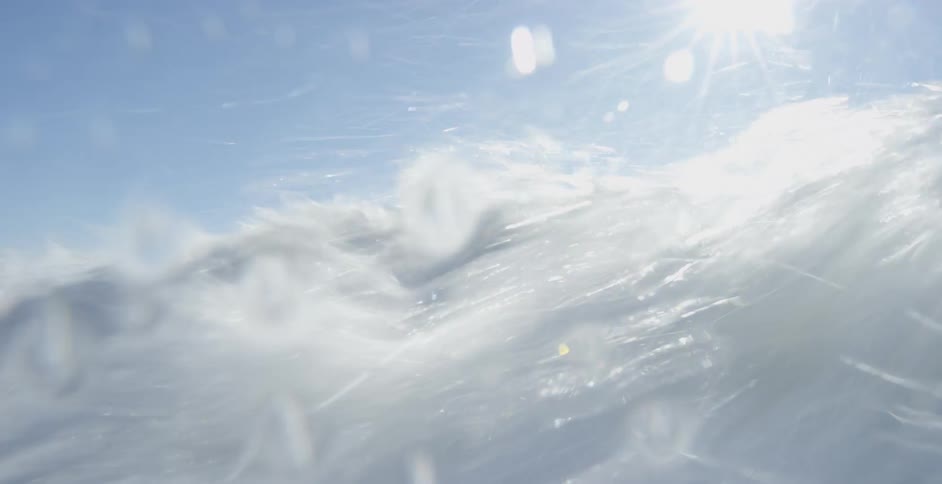 A man swimming out in the water with his surf board gets hit with a large wave and goes underwater