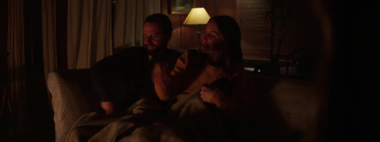 A husband and wife are sitting on a couch together at night