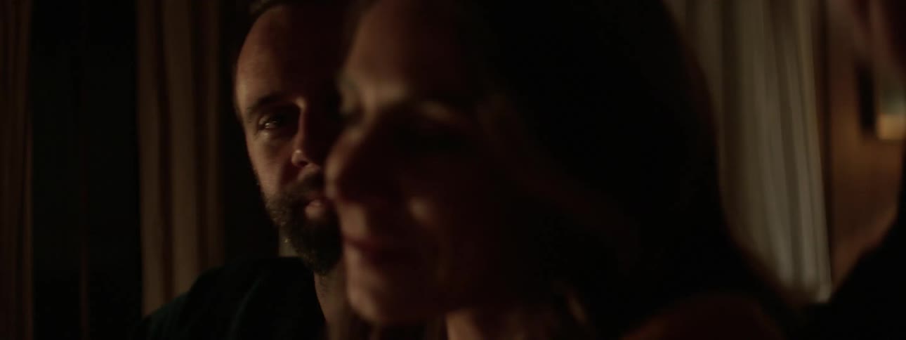 A man and woman sit down inside a house and then the man pulls the woman close as he puts his arm around her
