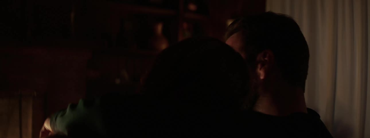 Man with a beard putting his arm around womans shoulder sits on a sofa watches a fireplace