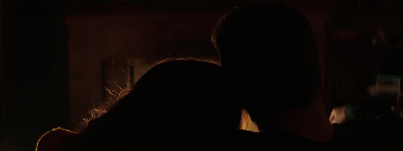A man and woman cuddle at home in front of a fireplace