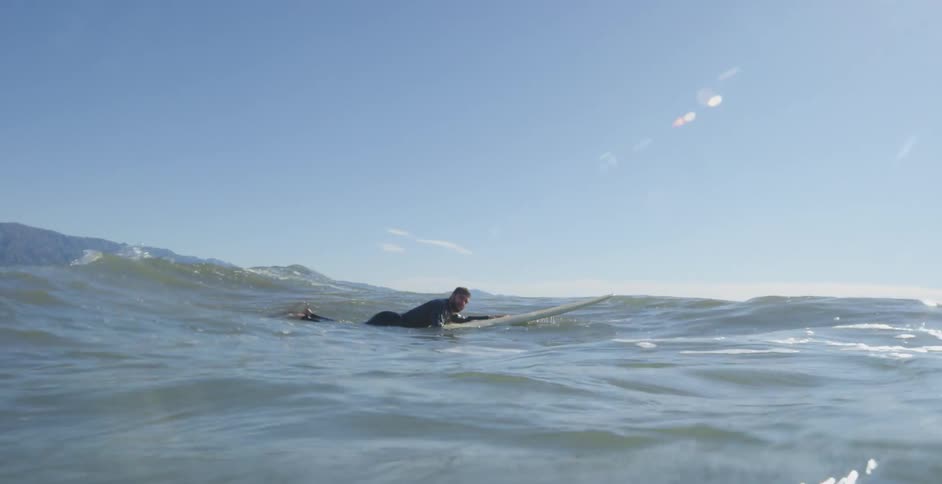 Surfer over a surfboard swims on the ocean waves at day