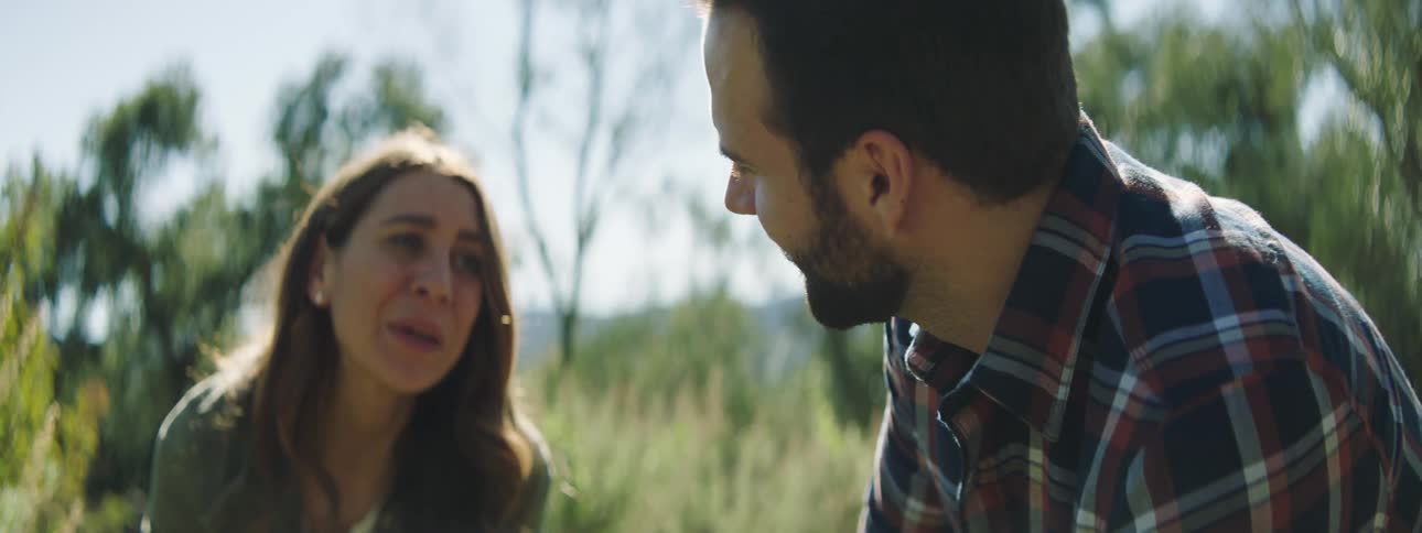 Man and woman talk while sitting outdoors in field backed by mountains
