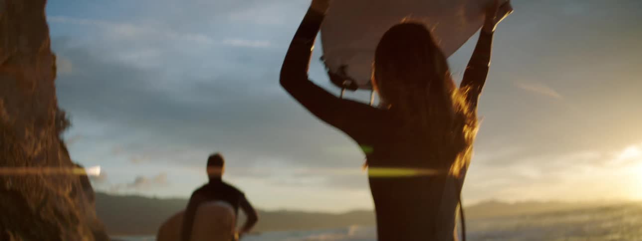 A man and woman walk along the beach carrying surfboards