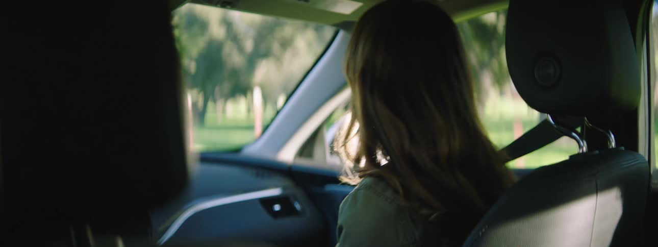 Woman sitting in the passenger seat of a car checks her phone and talks to the pilot