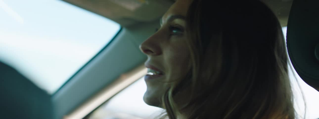 A woman in a car with landscape the sky and clouds in the background